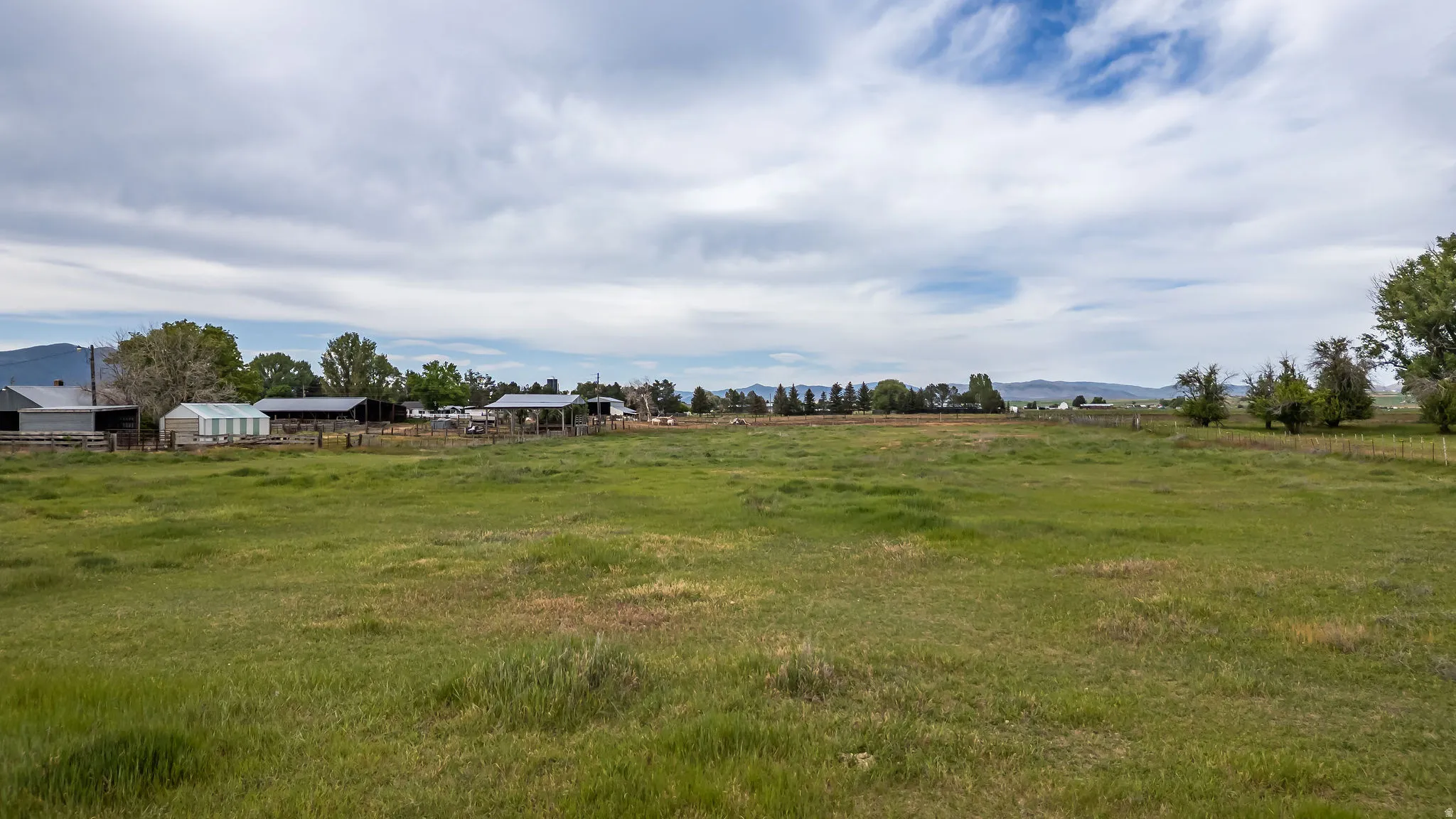 Expansive green pasture with distant mountains and multiple outbuildings, including a greenhouse and barn structures