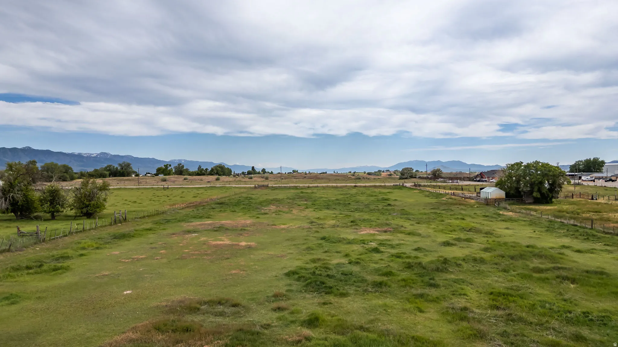Expansive green acreage featuring a wire fence perimeter and distant mountain scenery