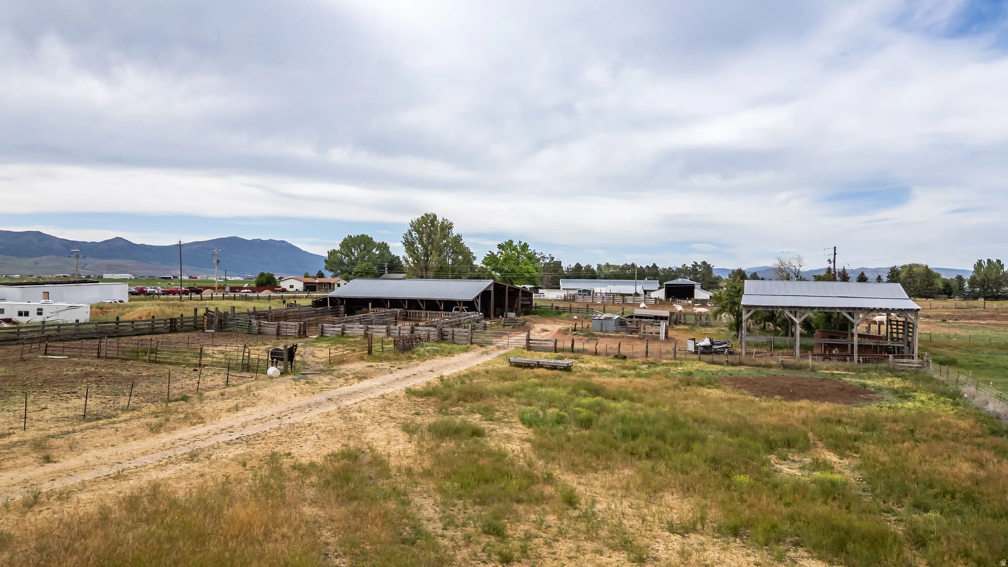 Expansive rural property featuring an unpaved driveway, multiple outbuildings, and extensive fencing