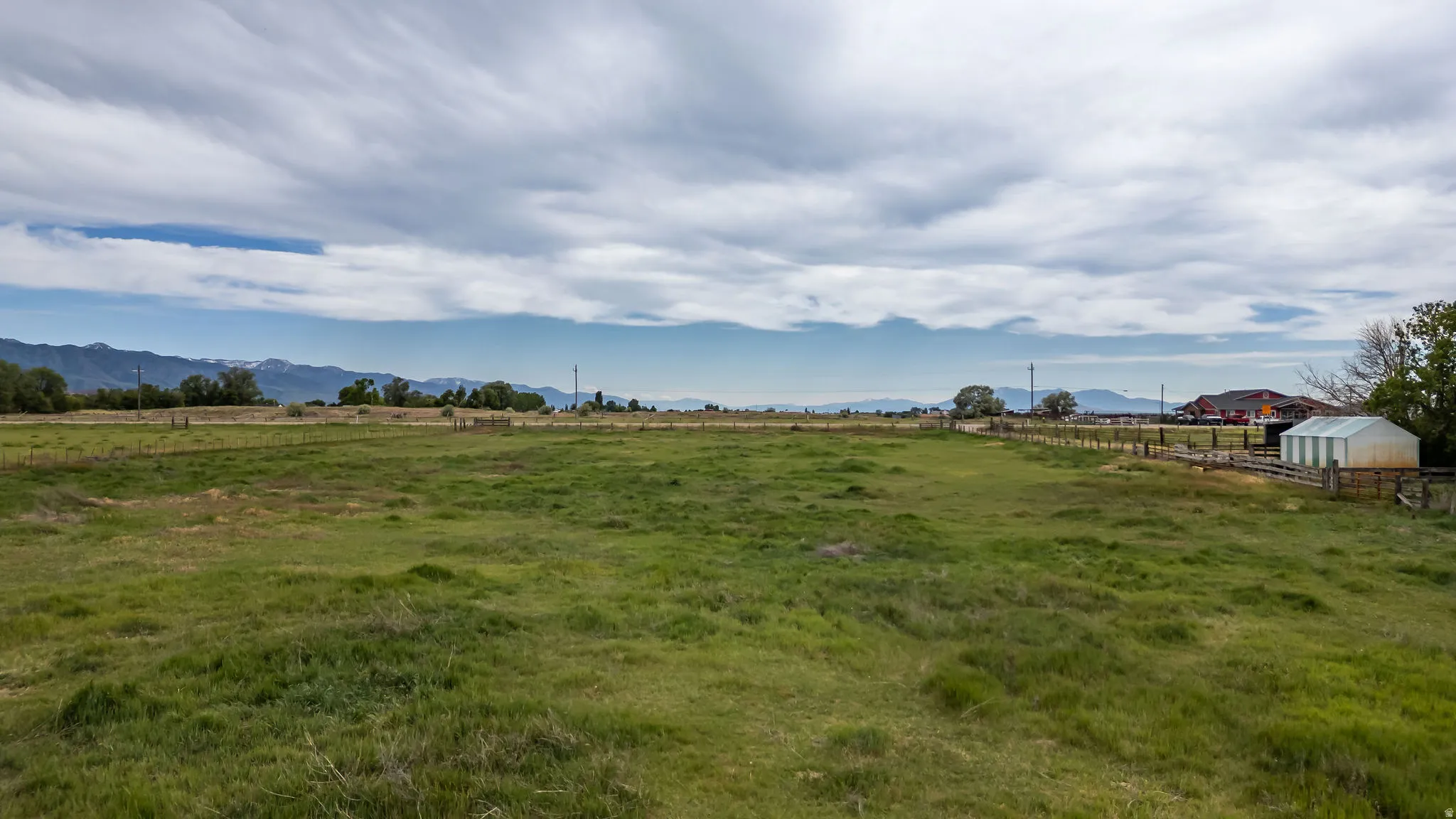 Expansive grass field with distant mountains and a white outbuilding