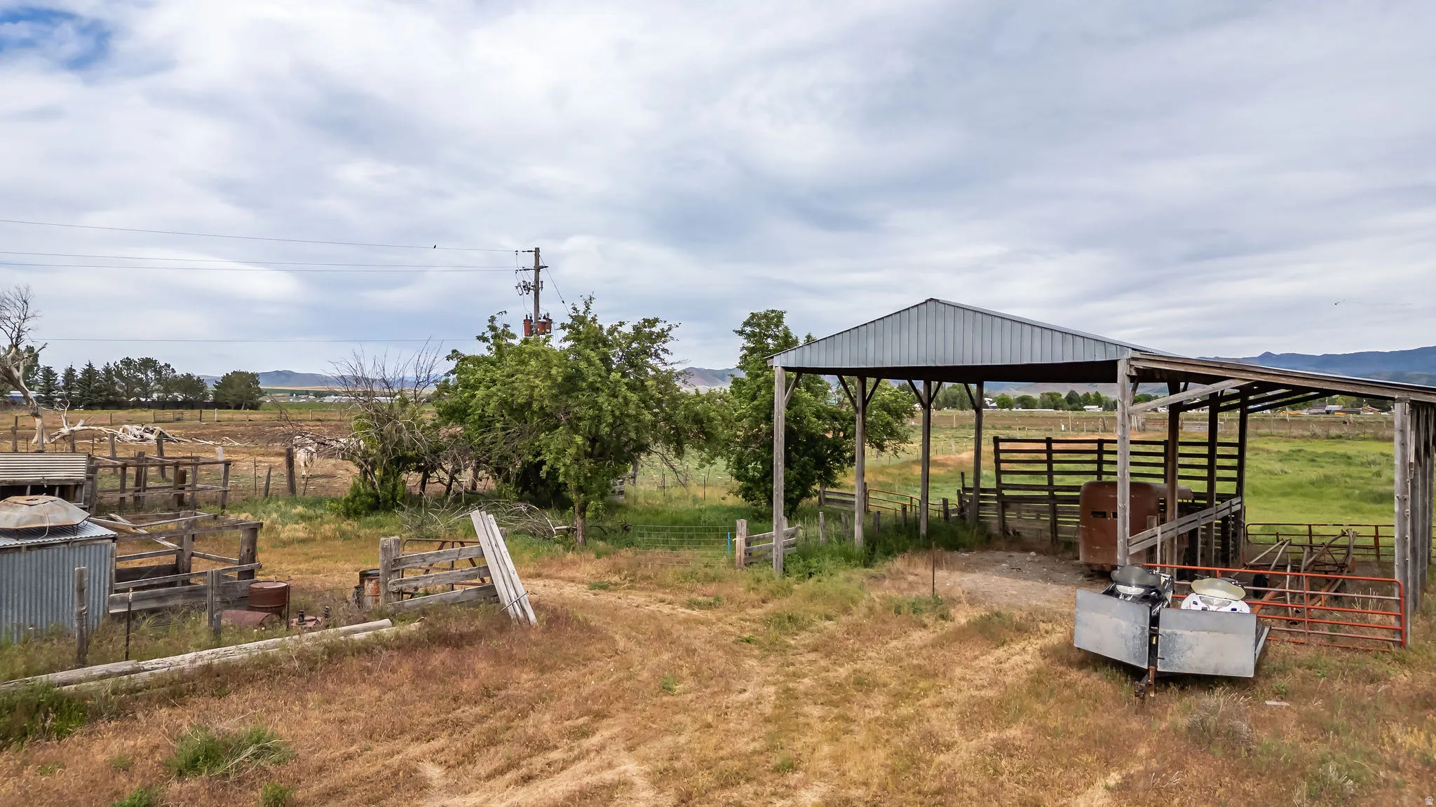 Expansive open-air barn with a metal roof and wood posts, featuring an interior wood fence
