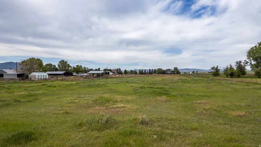 Expansive green pasture with distant mountains and multiple outbuildings, including a greenhouse and barn structures