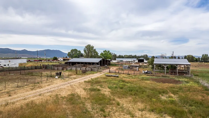 Expansive rural property featuring an unpaved driveway, multiple outbuildings, and extensive fencing