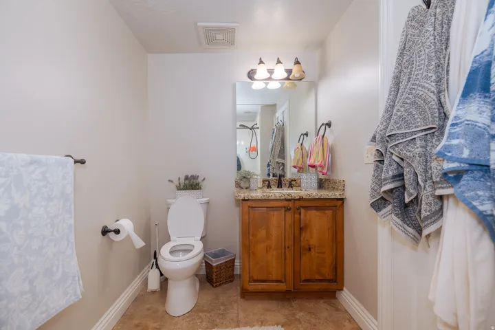 Bathroom featuring a wood-finish vanity with a granite-style countertop, a rectangular mirror, and a three-bulb vanity light fixture