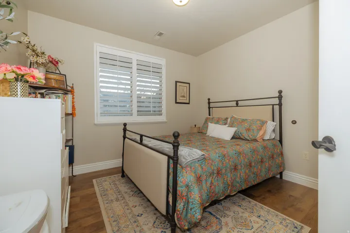Bedroom featuring wood-finish flooring, a window with white plantation shutters, and light neutral wall paint