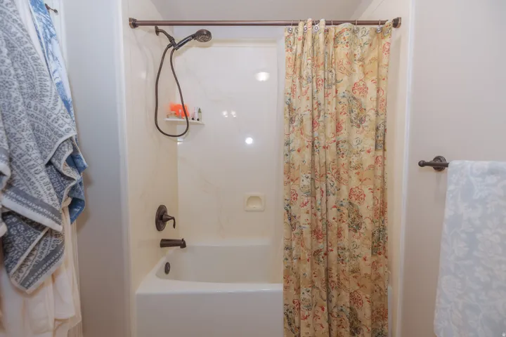 Bathtub and shower combination featuring a white surround and bronze-finish fixtures