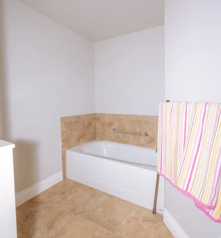 Bathtub with neutral-toned tiled surround and a stainless steel grab bar