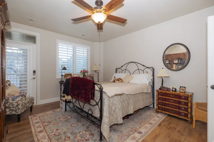 Bedroom featuring wood-finish flooring, a ceiling fan with integrated lighting, and a window with plantation shutters