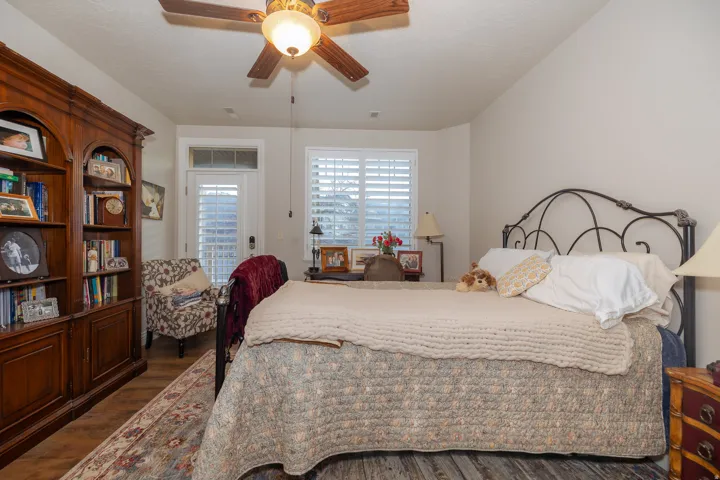 Bedroom featuring wood-finish flooring, a built-in wooden bookcase, and a ceiling fan with integrated lighting