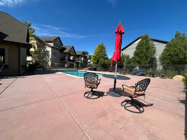 Outdoor swimming pool area featuring a red concrete patio, black metal fencing, and surrounding residential buildings with various exterior finishes
