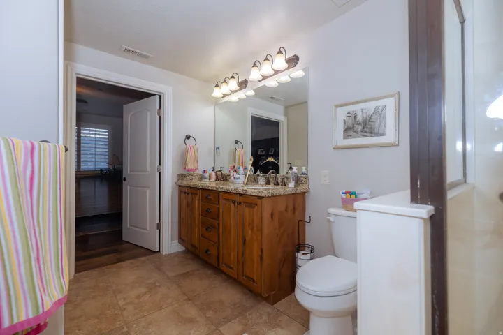 Bathroom featuring a wood-finish vanity with a granite-style countertop, dual sinks, and a large mirror