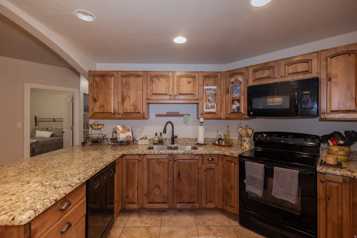 Kitchen featuring wood cabinetry, granite countertops, tile flooring, a black oven range, and a built-in microwave