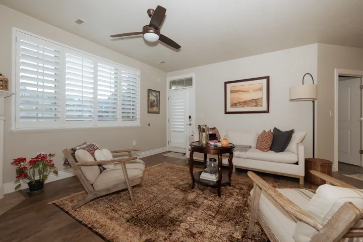 Living area with wood-finish flooring, white plantation shutters, a ceiling fan, and light-toned walls