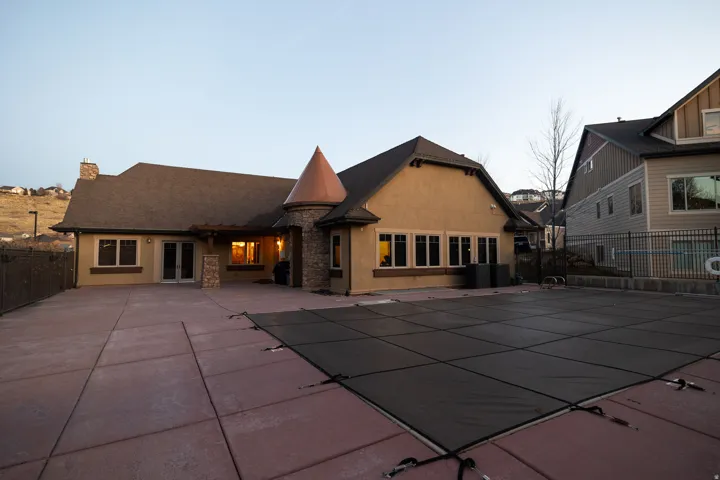 Rear exterior featuring a covered patio, extensive concrete decking, and a pool with a safety cover