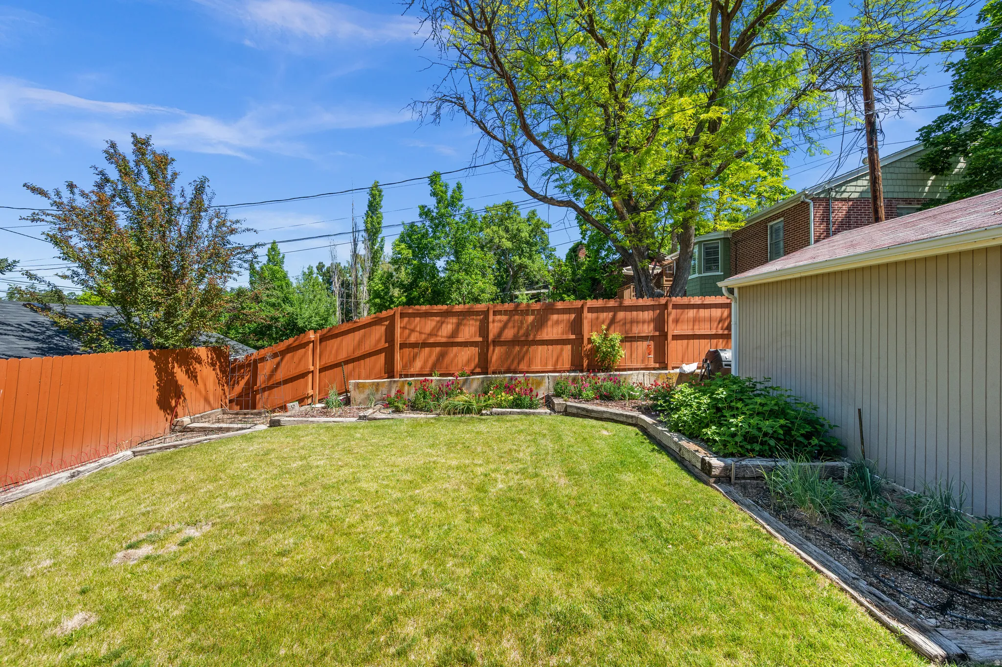 Sloping backyard featuring a vibrant lawn, wood privacy fencing, and established perimeter plantings