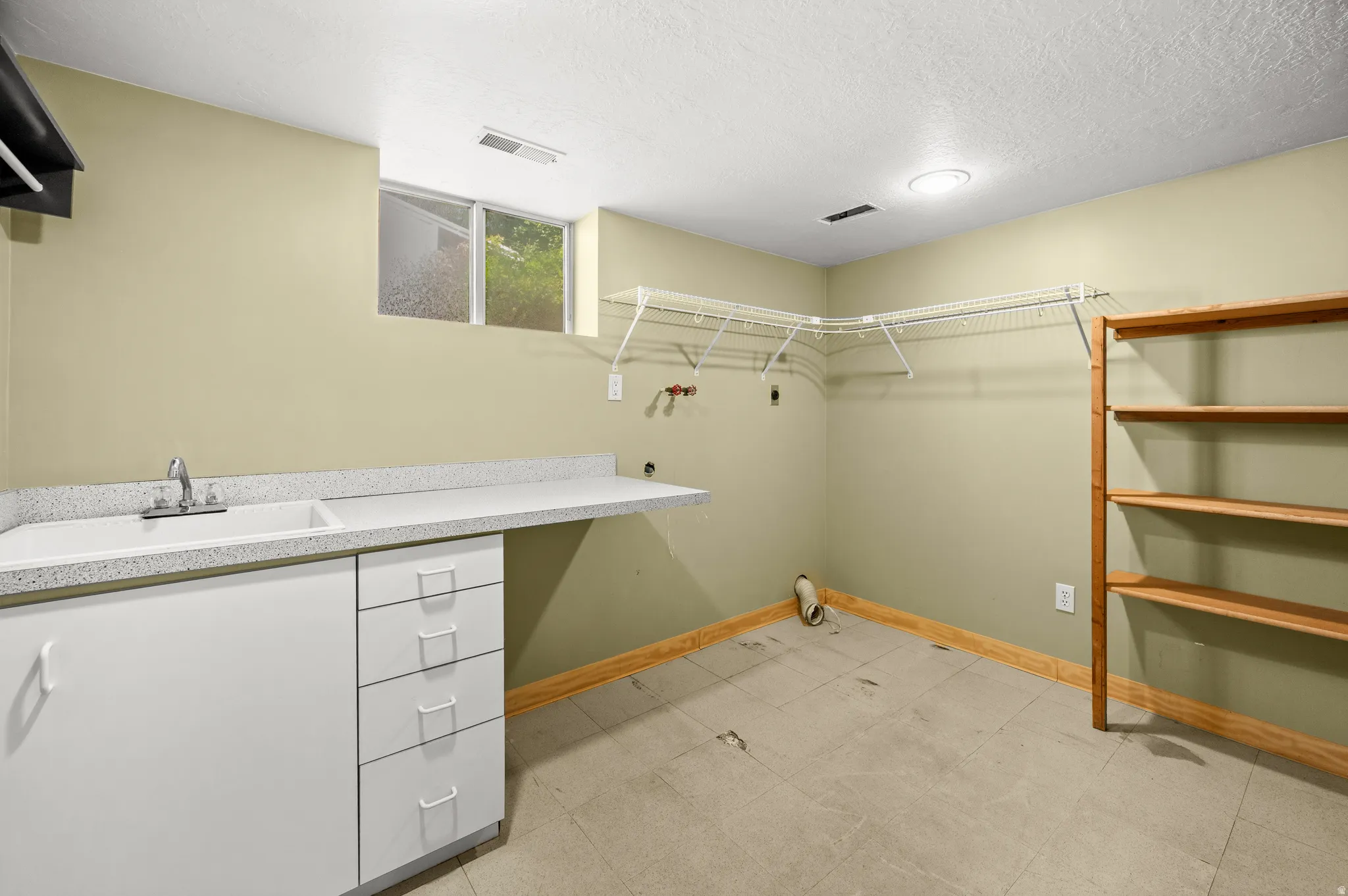 Utility room featuring a built-in sink with a countertop, white cabinetry with drawers, tile flooring, and a window for natural light