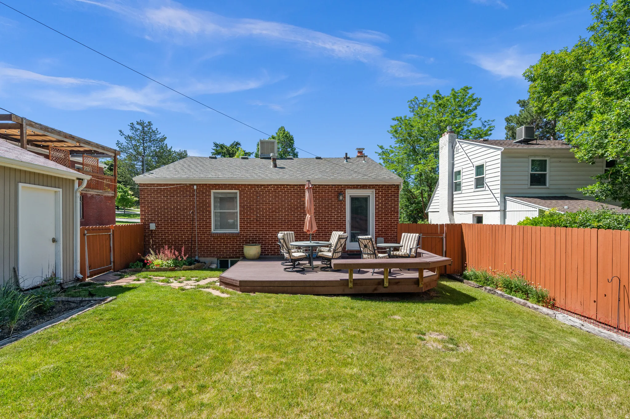Manicured lawn with a circular wood deck, brick exterior, and wood fencing