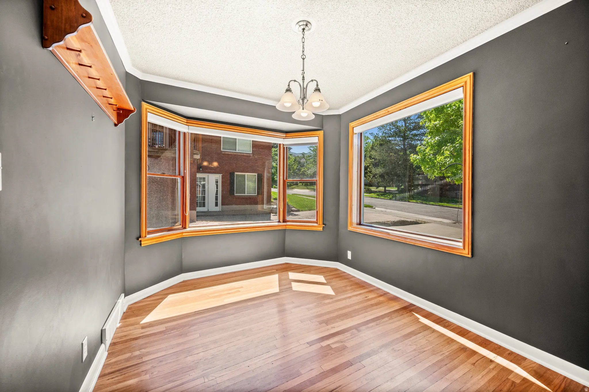 Hardwood flooring throughout, featuring a bay window, an additional large window, and a ceiling-mounted light fixture