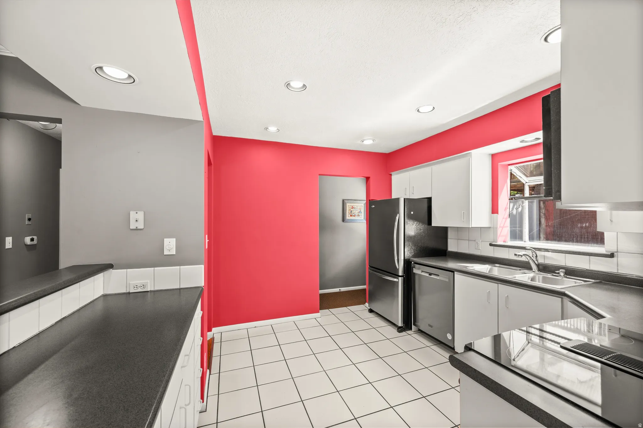 Kitchen featuring white tile flooring, stainless steel appliances, white cabinetry, dark countertops, and recessed lighting