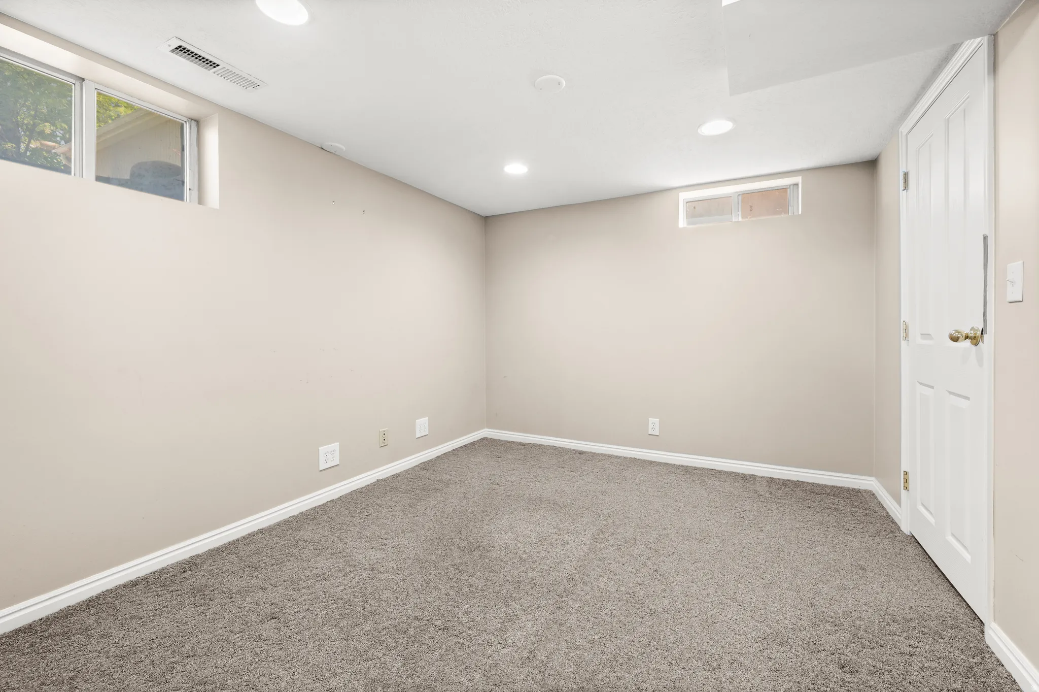 Neutral-toned room featuring light gray carpet, recessed lighting, white baseboards, and a white paneled door with brass hardware