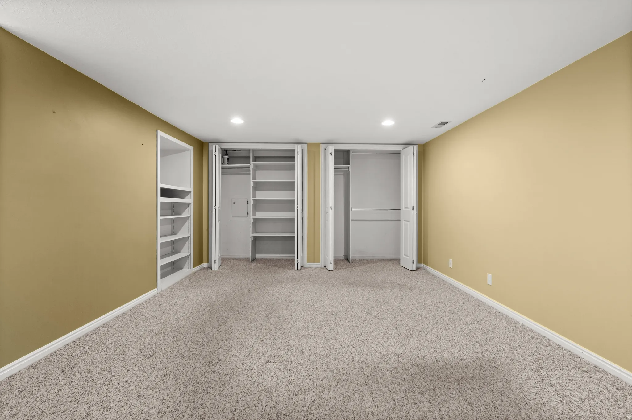 Carpeted room featuring built-in shelving, two bifold door closets, and recessed lighting