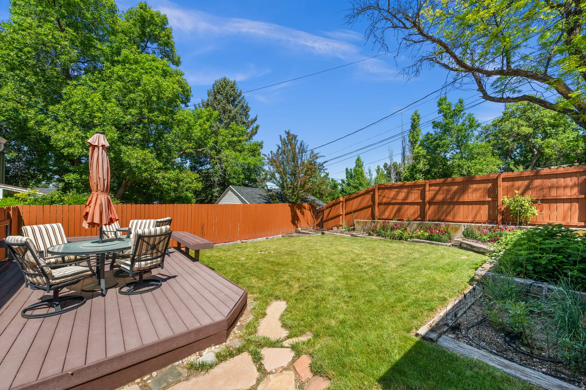 Expansive backyard featuring a composite deck, stone paver path, manicured lawn, and raised garden beds with established plantings