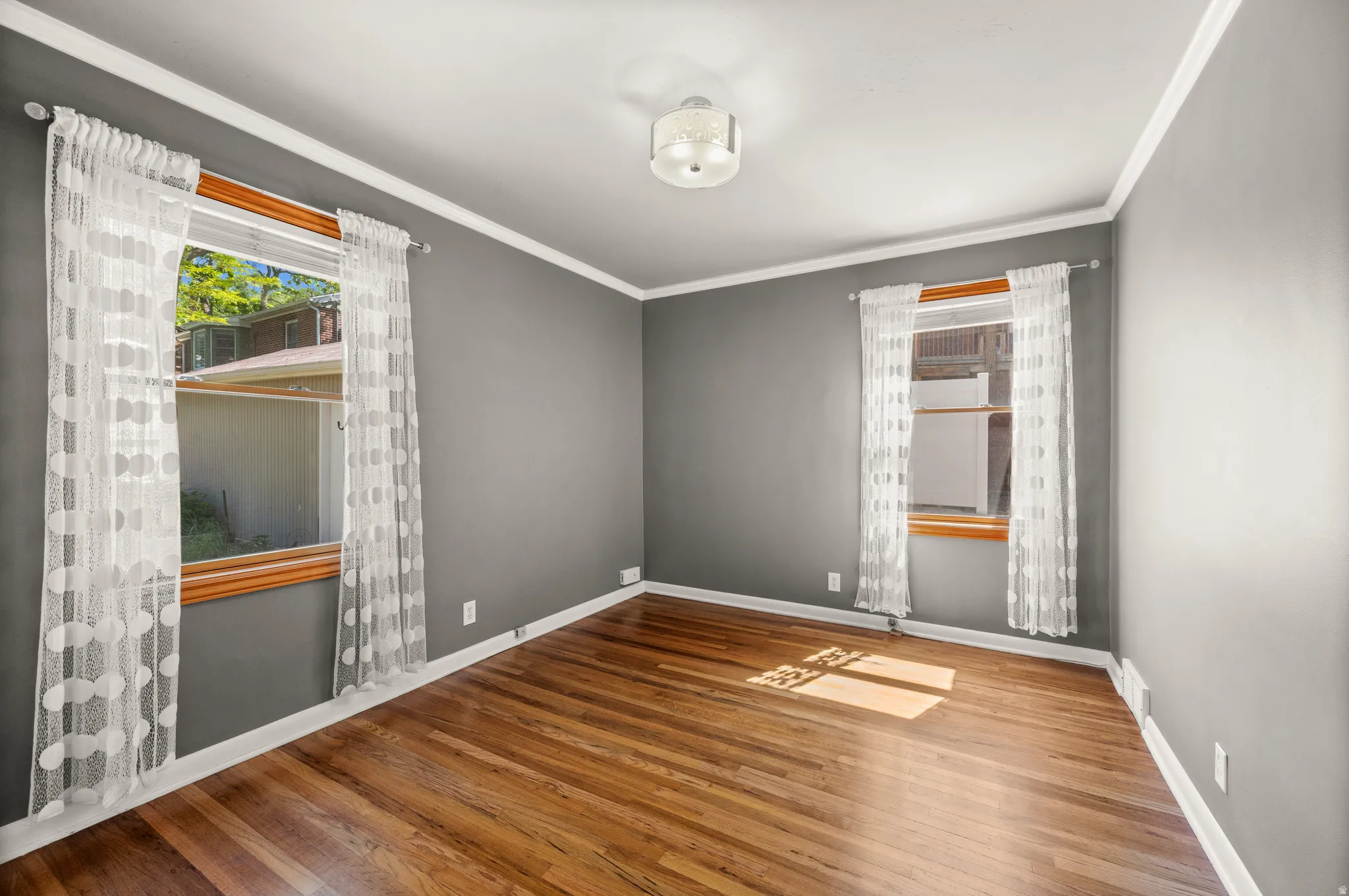 Interior space featuring wood-finish flooring, two large windows with wood trim, a ceiling-mounted light fixture, and crown molding