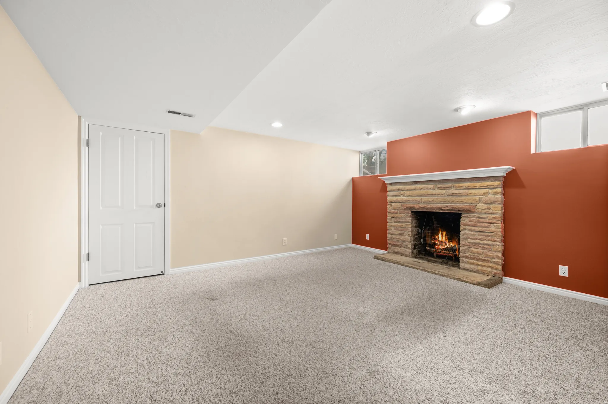 Stone-clad fireplace with a classic mantel, recessed lighting, neutral carpeting, and a four-panel interior door