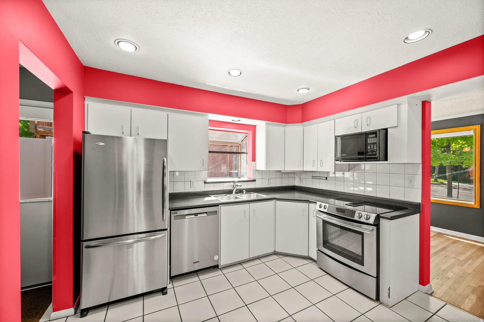 Kitchen featuring stainless steel appliances, white cabinetry, dark countertops, white tile flooring, and recessed lighting