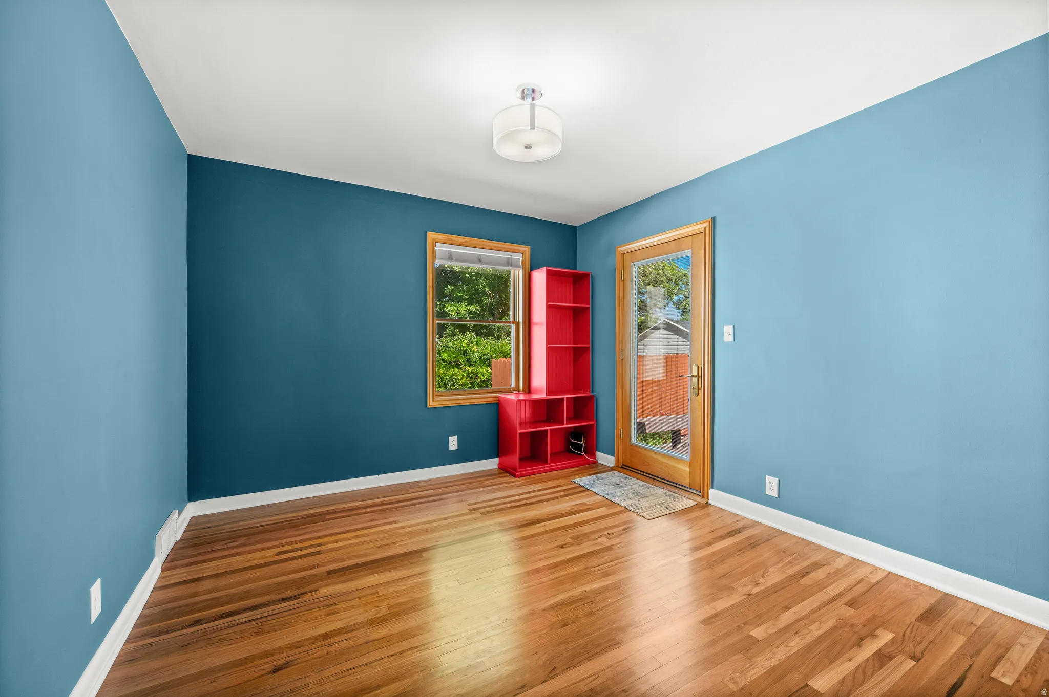 Hardwood flooring throughout featuring a transom window, a single exterior door with a glass insert, and a flush mount ceiling light fixture