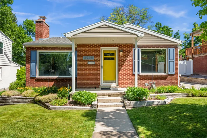 Brick facade home featuring a prominent yellow entry door, white trim, and a covered porch