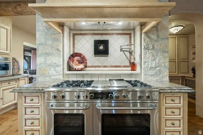 Stainless steel range with double ovens set into a stone and wood-finish range hood