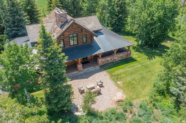 Log cabin-style residence featuring a prominent stone chimney, wood-shake roof, and a covered front porch with stone pillars