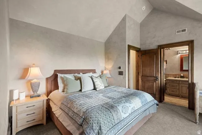 Vaulted ceilings and textured wall finishes define this room, featuring a wood-finish door and a visible en-suite bath with a wood-finish vanity