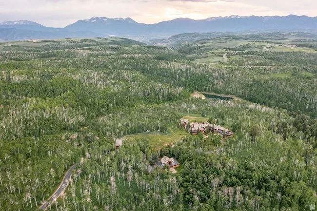 Expansive forested landscape featuring multiple structures, a winding paved road, and a calm body of water