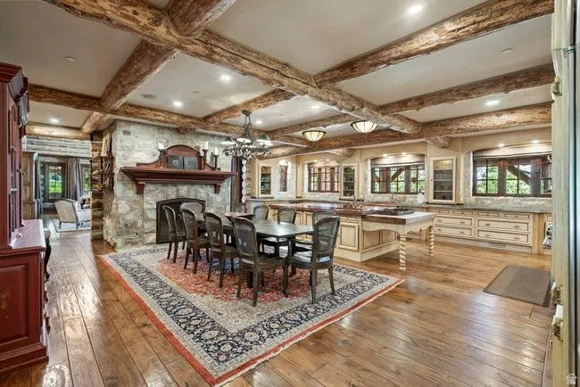 Kitchen and dining area featuring wood-finish flooring, exposed wood beams, a stone fireplace, cream cabinetry, and recessed lighting