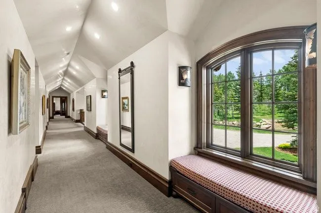 Hallway featuring an arched window, a built-in window seat with storage, decorative wall sconces, recessed lighting, and wood-finish trim