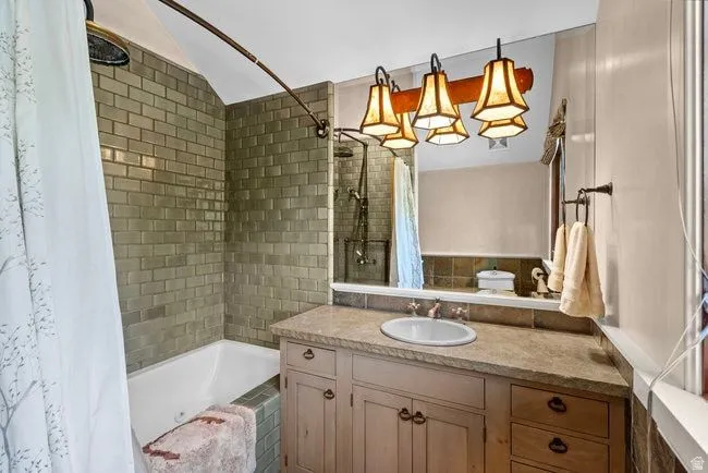 Bathroom featuring a tub/shower combination with subway tile surround, a single vanity with a stone-finish countertop, undermount sink, and wood-finish cabinetry