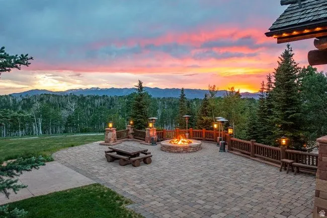 Expansive paver patio featuring a built-in stone fire pit, wood railing, and stone pillars