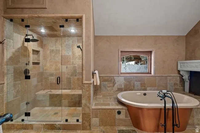Stone tile bathroom featuring a walk-in shower with a built-in bench, a rain showerhead, a hand-held shower, and a copper-clad soaking tub with an antique-style faucet