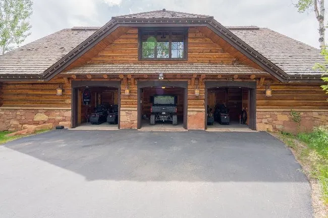 Three-bay garage with wood siding and stone accents, featuring a shingle roof, a second-story window, and exterior wall lanterns