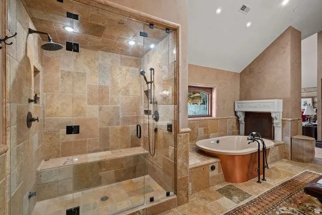 Spacious bathroom featuring a glass-enclosed shower with stone tile, a built-in shower bench, and multiple shower heads