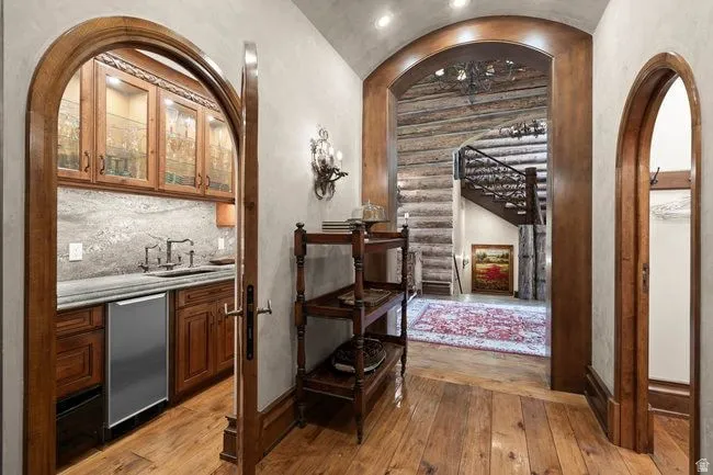 Archways frame a wet bar with wood cabinetry, glass-front upper cabinets, a stone countertop, and a stainless steel undercounter refrigerator