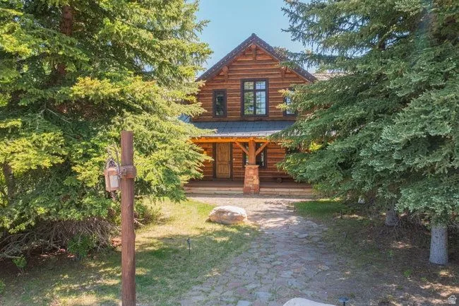 Log cabin style exterior featuring a covered porch, stone column accents, and a dark shingle roof