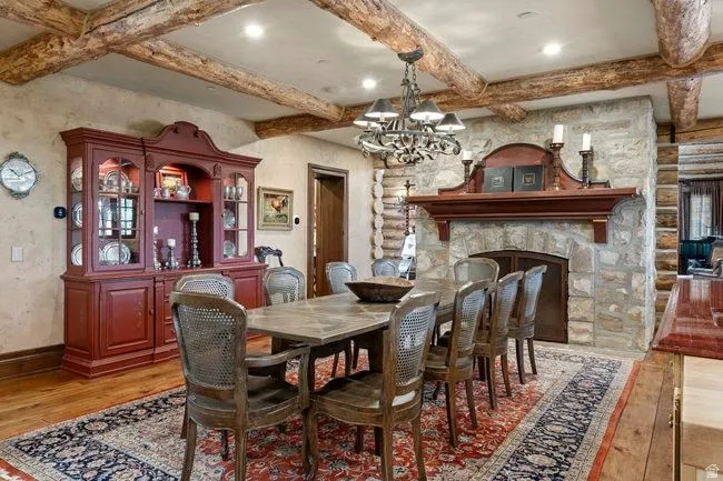 Dining area featuring a stone fireplace with a wood mantel, exposed log ceiling beams, and wood-finish flooring