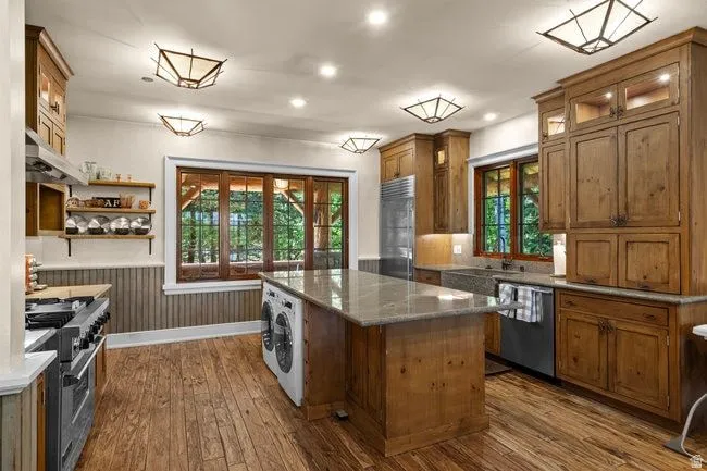 Spacious kitchen featuring wood-finish flooring, custom wood cabinetry, granite countertops, and stainless steel appliances