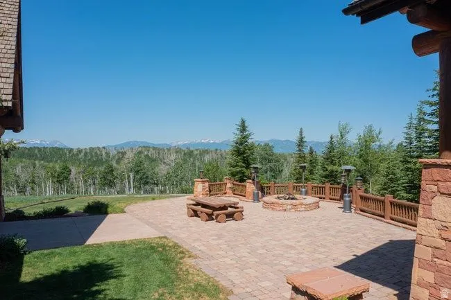 Expansive paver patio featuring a stone fire pit, wood railing, and stone pillars