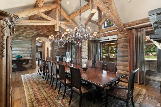 Vaulted ceiling with exposed wood beams, log wall construction, wood-finish flooring, ornate chandelier, and multiple window exposures