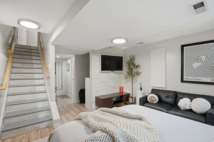 Finished lower level featuring a modern staircase with light wood handrails, recessed lighting, and wood-finish flooring