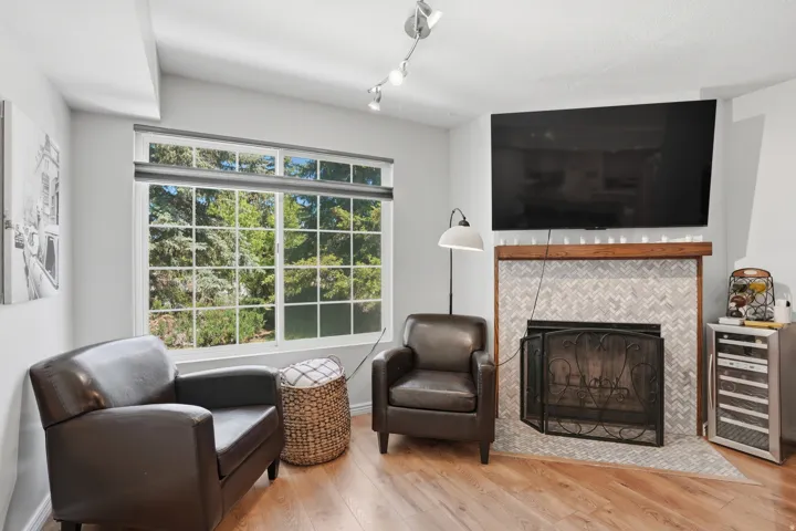 Living area featuring a spacious window, light wood-finish flooring, and a fireplace with a herringbone tile surround and wood mantle